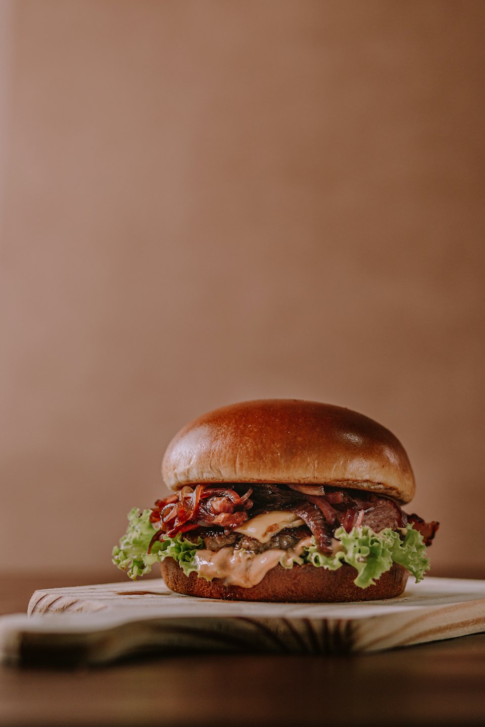 Gourmet burger with beef, cheese, lettuce, and onions on a brioche bun.
